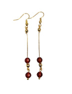Gold-plated dangle earrings with deep red agate faceted beads on a white background.