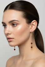 model wearing Gold-plated dangle earrings with deep red agate faceted beads on a white background.
